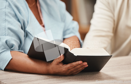 Image of Hands, bible and books with a senior couple reading a book together in their home during retirement. Jesus, faith or belief with a man and woman praying to god in their house for spiritual bonding