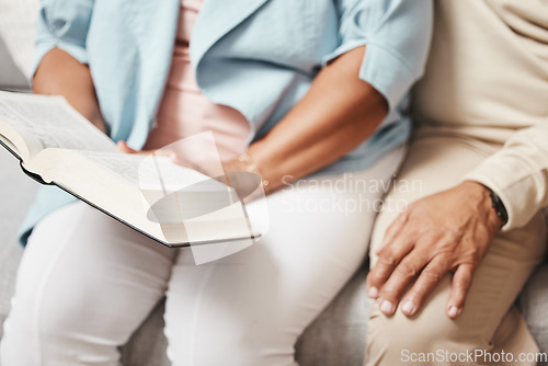 Image of Hands, bible and praying with a senior couple reading a book together in their home during retirement. Jesus, faith or belief with a man and woman in prayer to god in a house for spiritual bonding