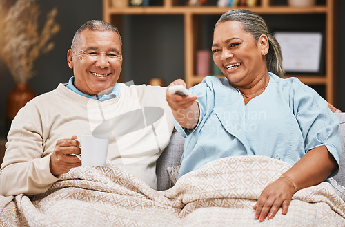 Image of Coffee, relax and old couple watching tv with blanket on sofa in home living room laughing at comic film. Retirement portrait, valentines love and happy elderly man and woman streaming on television.