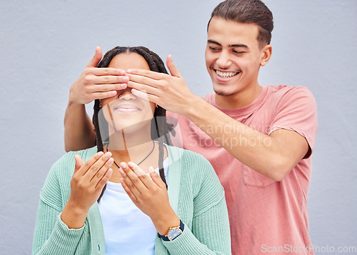 Image of Wow, surprise or hands and a couple on a gray background outdoor with a man covering the eyes of his girlfriend. Diversity, hands or dating with a woman being surprised by her boyfriend on a wall