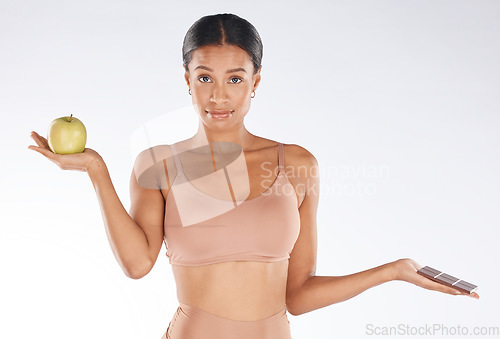 Image of Black woman, studio and portrait for apple, chocolate and decision for health, body and nutrition by background. Gen z model, underwear or choice for diet, fruit or candy for thinking of cheat day