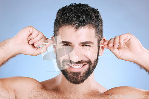 Image of Cleaning, ear and man with cotton bud in studio for hygiene, grooming and beauty routine on blue background. Earwax, product and guy model in cosmetic, luxury and wax, removal or stick while isolated