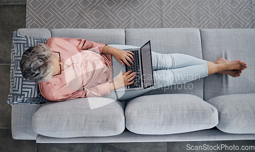 Image of Senior woman, laptop and sofa above relaxed in the living room checking email, typing or writing at home. Elderly female freelancer or writer relaxing on lounge couch working or reading on computer