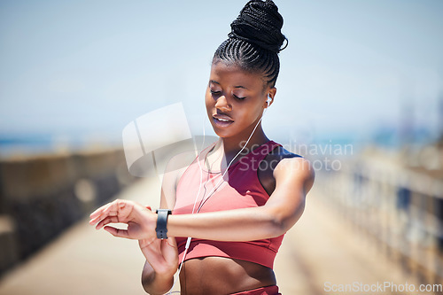 Image of Black woman, fitness and checking watch for time or monitoring performance after running exercise outside. African American female runner looking at wristwatch with earphones for tracking workout