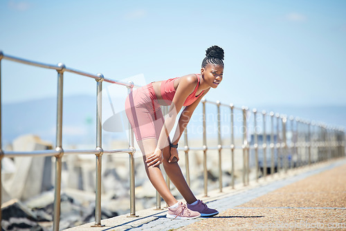 Image of Fitness, tired and black woman breathing after an outdoor running workout on the beach promenade. Sports, health and exhausted African female on a break with fatigue after cardio exercise or training