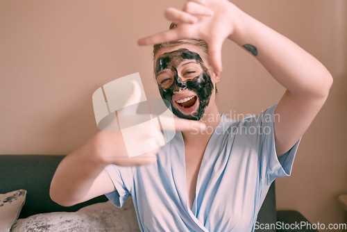 Image of Self care, face mask and funny woman in her home, house or apartment doing morning beauty routine and hand gesture. Portrait, relax and female taking picture frame or sign for skincare using charcoal