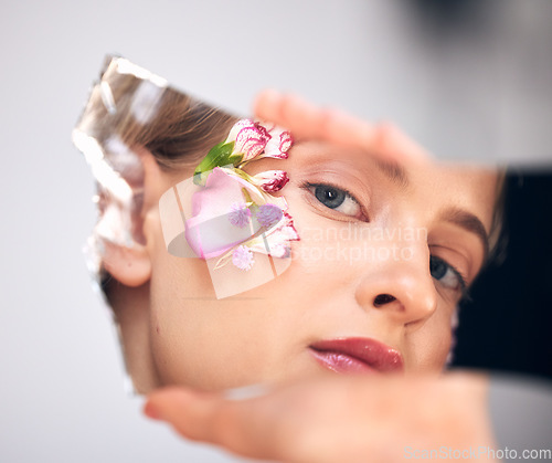 Image of Portrait, skincare and woman with reflection, flower and cosmetics on grey studio background. Face, female and lady with mirror, plants and floral for decoration, makeup and natural dermatology