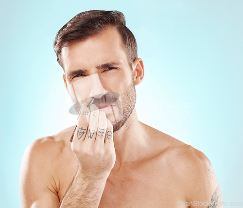 Image of Man with tweezer, grooming nose hair and morning routine for beauty and skincare isolated on blue background. Face, aesthetic and pain, plucking facial hairs, male model with tattoo on hand in studio