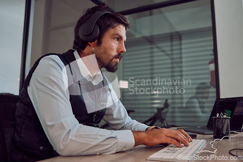 Image of Headphones, programmer keyboard and man typing, coding or programming online at night. Information technology, computer and male employee or coder working on software while streaming music or radio.