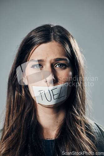 Image of Woman, face and tape on mouth for fuel prices, ecumenic struggle or financial crisis against gray studio background. Portrait of female activist with covered lips in silence, speech or voice message