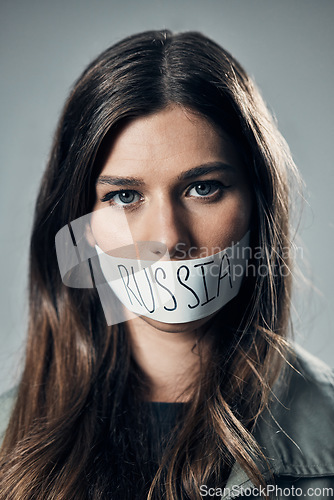 Image of Woman, face and protest with mouth tape in Russia for cold war, armageddon or doomsday against a gray studio background. Portrait of female activist or secret Russian agent or refugee in silence