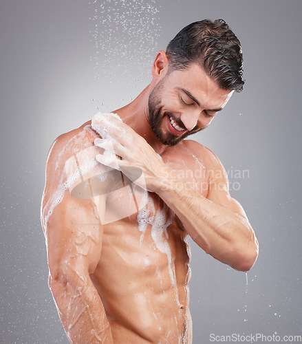 Image of Shower, sponge and man with water in studio on gray background for wellness, grooming and beauty. Skincare, bathroom hygiene and happy male smile for washing body, cleaning and soap for healthy skin