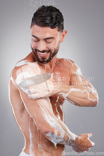 Image of Man, shower and cleaning with soap with studio background, smile and hygiene to start morning. Model, washing and happy with water drops, wellness and healthy skincare process in bathroom for health