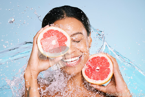 Image of Beauty, grapefruit and skin care with a woman for healthy skin and diet on a blue background. Face of aesthetic model person with water splash and fruit for sustainable facial health and wellness