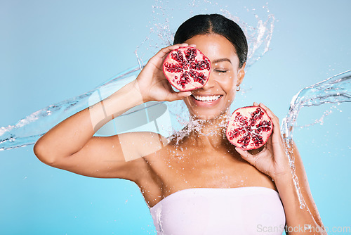 Image of Skincare, beauty and woman with a pomegranate for healthy food and skin on a blue background. Face of aesthetic model person with water splash and fruit for sustainable facial health and wellness