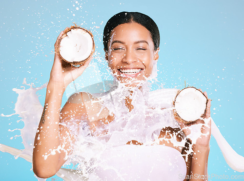 Image of Beauty, skin care and woman with coconut for healthy skin and diet on a blue background. Face of happy aesthetic model person with milk splash and fruit for sustainable facial health and wellness