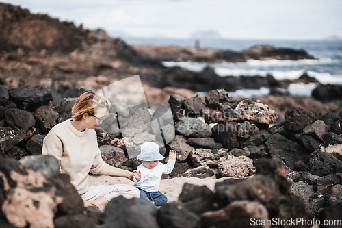 Image of Mother playing his infant baby boy son on sandy beach enjoying summer vacationson on Lanzarote island, Spain. Family travel and vacations concept.