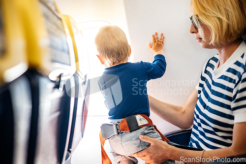 Image of Mom and child flying by plane. Mother holding and playing with her infant baby boy child in her lap during economy comercial flight. Concept photo of air travel with baby. Real people.