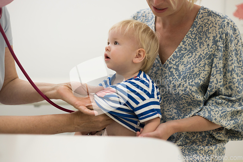 Image of Infant baby boy child being examined by his pediatrician doctor during a standard medical checkup in presence and comfort of his mother. National public health and childs care care koncept.