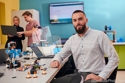 Image of A man sitting in a robotics laboratory while his colleagues in the background test new, cutting edge robotic inventions.