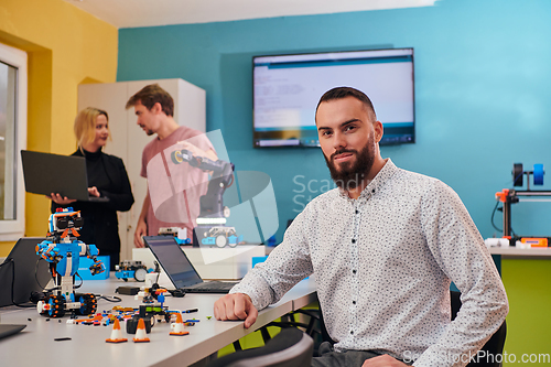 Image of A man sitting in a robotics laboratory while his colleagues in the background test new, cutting edge robotic inventions.