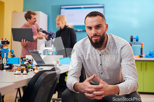 Image of A man sitting in a robotics laboratory while his colleagues in the background test new, cutting edge robotic inventions.