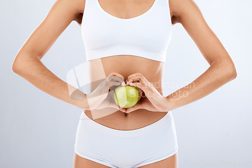 Image of Digestion, apple and woman stomach with hands in heart shape for nutrition, detox diet and studio background. Fruits, wellness and healthy abdomen body with care, love and lose weight for strong gut