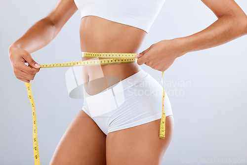 Image of Weightloss, health and woman with measuring tape in a studio for her diet, exercise or wellness. Fitness, body and healthy slim female model checking the measurement of her waist by a gray background