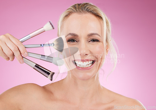 Image of Portrait, makeup and cosmetic brushes with a mature woman in studio on a pink background to promote a product. Face, happy and cosmetics with an attractive older female posing for beauty treatment