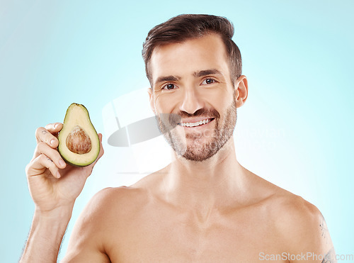 Image of Man, skincare and studio portrait with avocado for health, nutrition and cosmetic wellness by blue background. Happy young model, fruit and healthcare for natural detox, facial skin glow or aesthetic