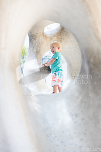 Image of Child playing on outdoor playground. Toddler plays on school or kindergarten yard. Active kid on stone sculpured slide. Healthy summer activity for children. Little boy climbing outdoors.