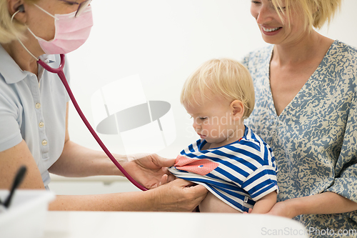 Image of Infant baby boy child being examined by his pediatrician doctor during a standard medical checkup in presence and comfort of his mother. National public health and childs care care koncept.