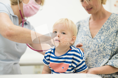 Image of Infant baby boy child being examined by his pediatrician doctor during a standard medical checkup in presence and comfort of his mother. National public health and childs care care koncept.