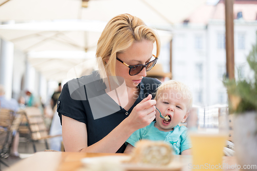 Image of Young mother relaxing together with her little child, adorable toddler girl, in summer outdoors cafe drinking coffee and eating muffin or cupcke. Family in love. Kid an beautiful woman.
