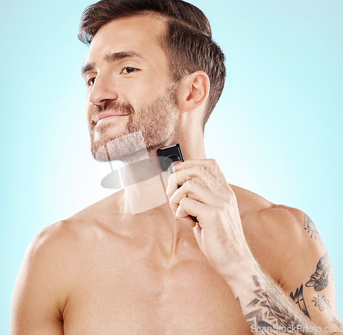 Image of Man, beard and shaving with trimmer in studio isolated on a blue background for hair removal. Haircare thinking, grooming and male model with electric shaver to shave for hygiene, health or wellness.