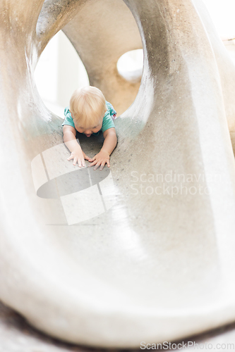 Image of Child playing on outdoor playground. Toddler plays on school or kindergarten yard. Active kid on stone sculpured slide. Healthy summer activity for children. Little boy climbing outdoors.