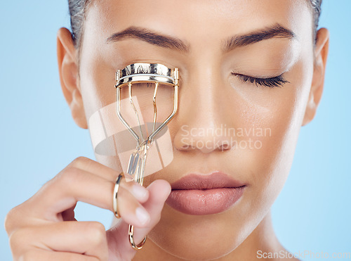 Image of Cosmetics, routine and woman with an eyelash curler isolated on a blue background in a studio. Skincare, beauty and face of model with a metal product for lashes, makeup and mascara on a backdrop