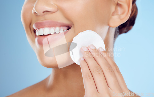 Image of Skincare, smile and woman with cotton pad on face, removing makeup or dirt removal with luxury skin product in studio. Dermatology, cosmetics and facial for happy model isolated on blue background.