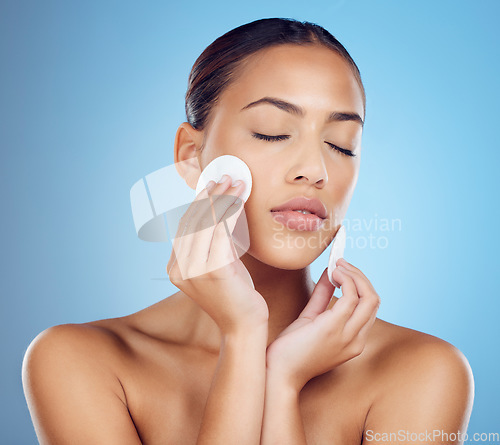 Image of Skincare, woman with cottonwool on face and eyes closed removing makeup or dirt with luxury skin product in studio. Dermatology, cosmetics and beauty spa facial for model isolated on blue background.