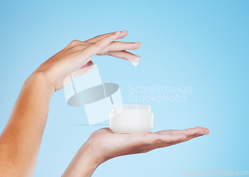 Image of Skincare, beauty and hands with face cream in studio for a natural, cosmetic or hydration skin routine. Self care, product and closeup of female with spf, sunscreen or facial creme by blue background