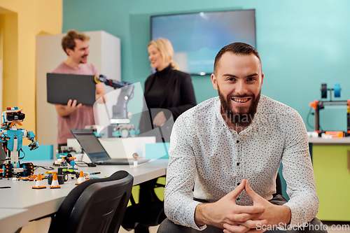 Image of A man sitting in a robotics laboratory while his colleagues in the background test new, cutting edge robotic inventions.