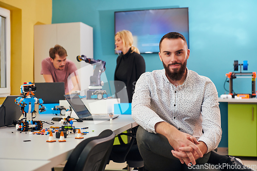 Image of A man sitting in a robotics laboratory while his colleagues in the background test new, cutting edge robotic inventions.