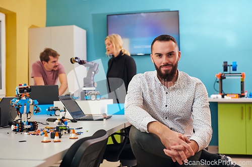 Image of A man sitting in a robotics laboratory while his colleagues in the background test new, cutting edge robotic inventions.