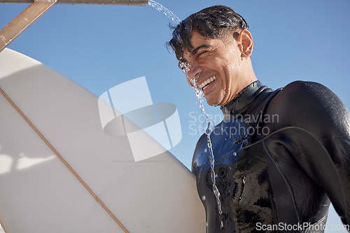 Image of Man, surfing and water shower at beach on face, smile or blue sky in summer, sunshine or ocean travel. Happy surfer cleaning body at tap for sea sports, relax holiday or vacation adventure in wetsuit