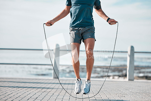 Image of Jump rope, fitness and man by a sea promenade with training, sports and exercise equipment. Health, jumping and body wellness of a athlete doing cardio jump for active lifestyle by the ocean