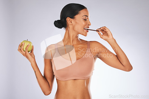 Image of Woman, studio and choice with chocolate, apple or cheating on diet with candy by gray background. Young gen z model, eating and smile with fruit, sweets and decision for health, wellness or nutrition