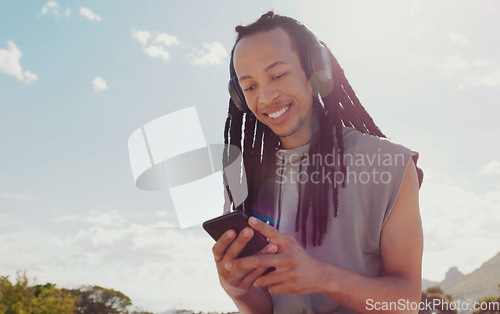 Image of Sky, black man and smartphone with headphones streaming music, online reading and podcast outdoor. African American male, guy and cellphone for social media, headset and listen to audio and sounds