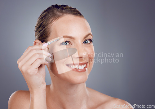 Image of Eyebrows, grooming and portrait of a woman with a tweezers isolated on a grey studio background. Beauty, treatment and happy model plucking hair from face for shaping and routine on a backdrop