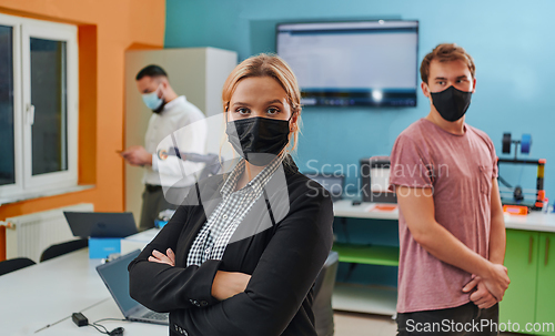 Image of A woman wearing a protective mask standing in a laboratory while her colleagues test a new robotic invention in the background.
