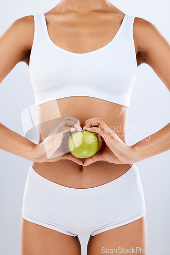 Image of Nutrition, apple and woman hands on stomach in heart shape for digestion, detox diet and studio background. Fruits, wellness and healthy abdomen body with care, love and lose weight for strong gut